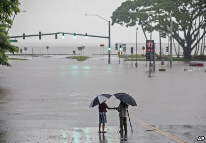 In this Aug. 23, 2018 file photo, people stand near flood waters from Hurricane Lane in Hilo, Hawaii. Some of Hawaii's most iconic beaches could soon be underwater. (Hollyn Johnson/Hawaii Tribune-Herald via AP, File)